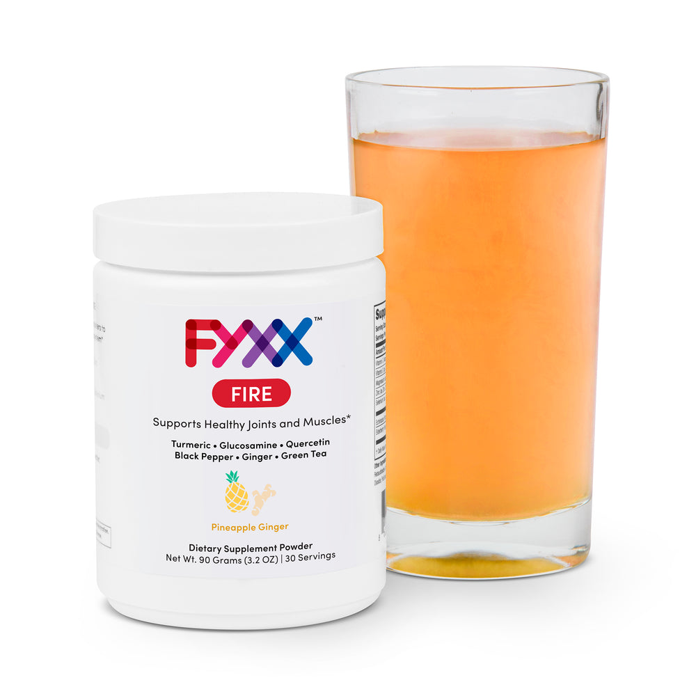 A jar of FYXX Fire dietary supplement powder sits next to a mixed and ready-to-drink glass. The pineapple ginger flavor can be seen in the orange color of the drink.