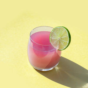 
                  
                    A bright pink drink with a lime wheel garnish sits against a yellow backdrop. The drink was made using the FYXX Epic Immunity Drink Mix.
                  
                