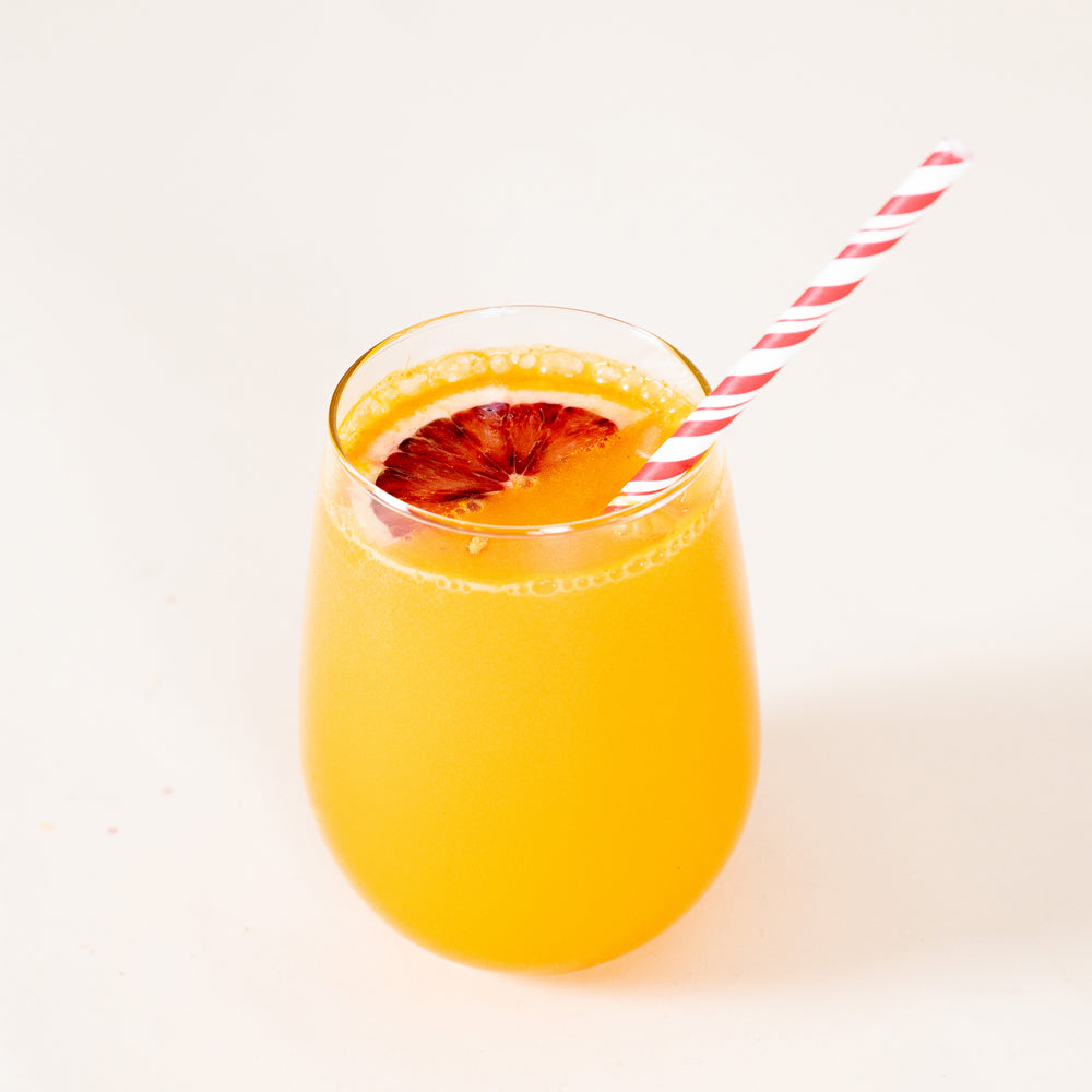 
                  
                    A bright yellow-orange drink with a blood orange wedge and red striped paper straw sits on a white table. The drink was made using the FYXX Fire Drink Mix.
                  
                