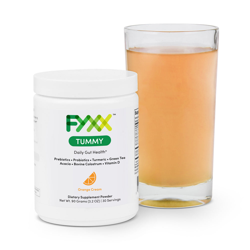 A jar of FYXX Tummy dietary supplement powder sits next to a mixed and ready-to-drink glass. The orange cream flavor can be seen in the orange color of the drink.