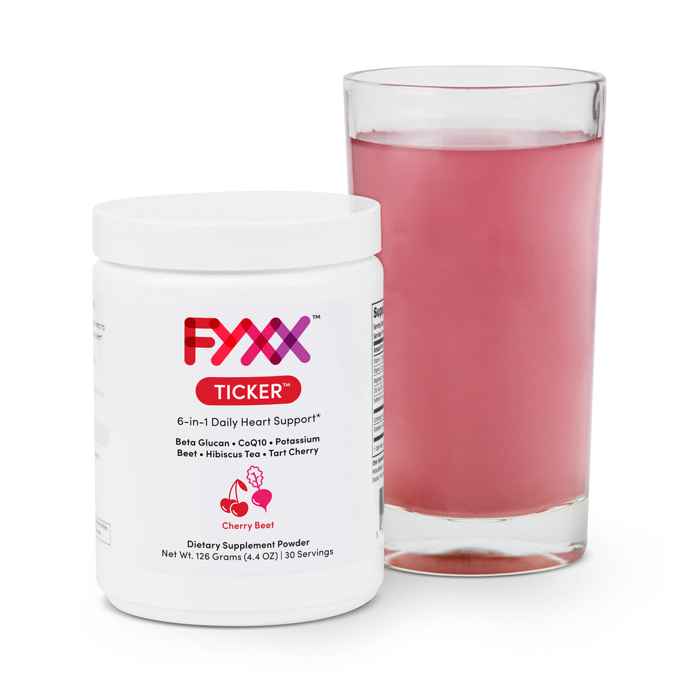 A jar of FYXX Ticker dietary supplement powder sits next to a mixed and ready-to-drink glass. The cherry beet flavor can be seen in the red color of the drink.